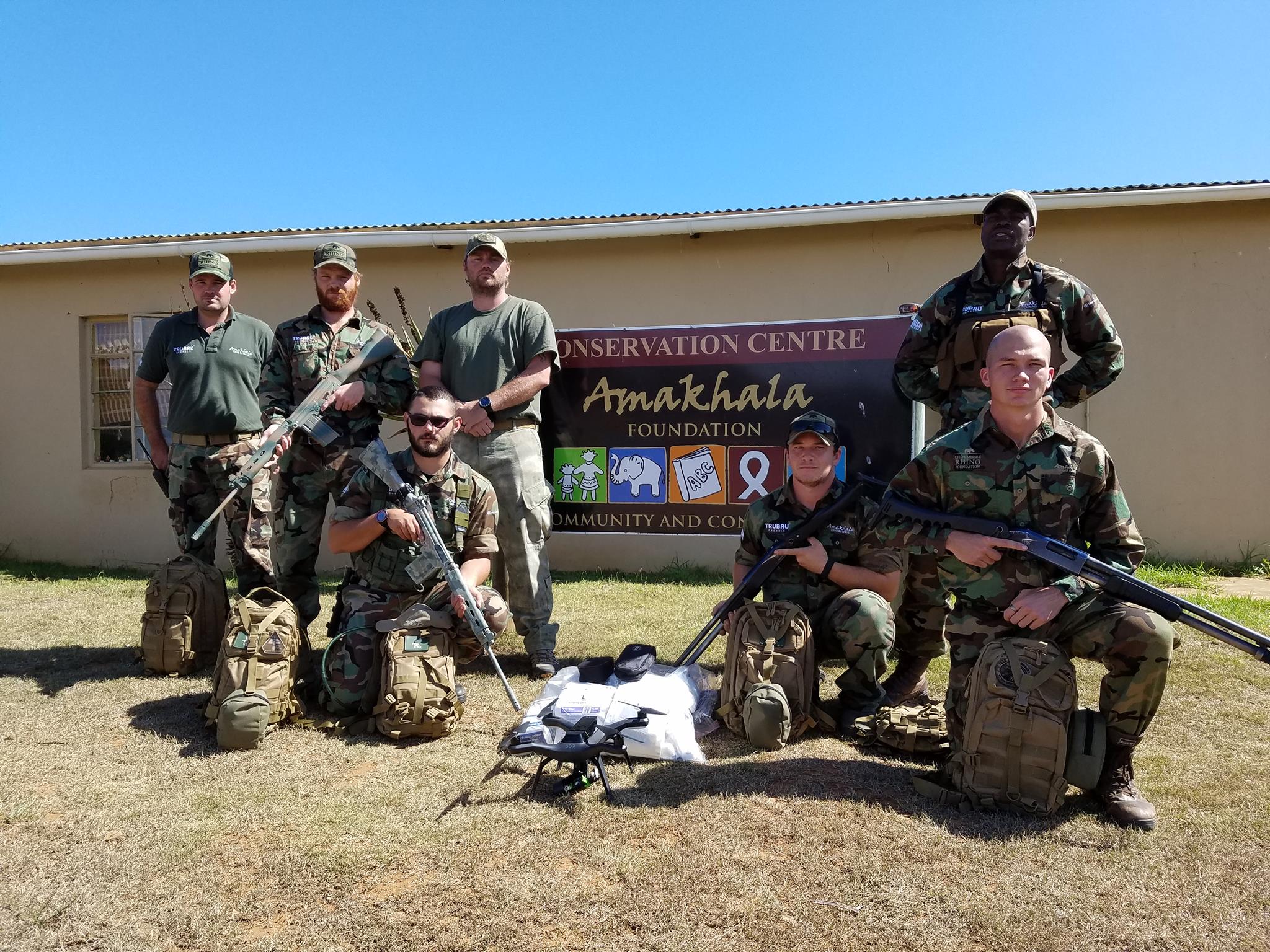seven rangers posing with equipment in front of a single-story building